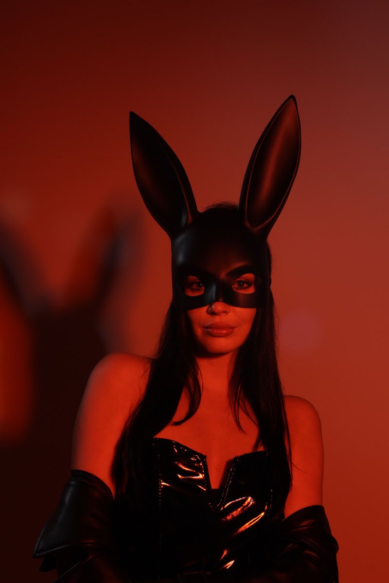 Illustrative stock portrait of an adult wearing a black rabbit mask against red lighting